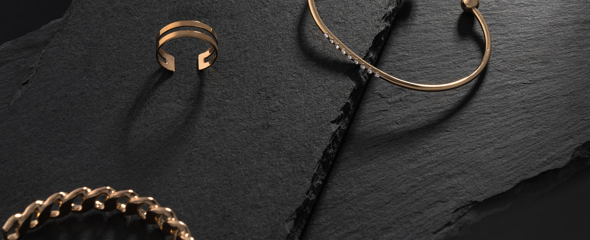 Gold plated bracelets with gemstones and chain links arranged on black stone, premium jewelry